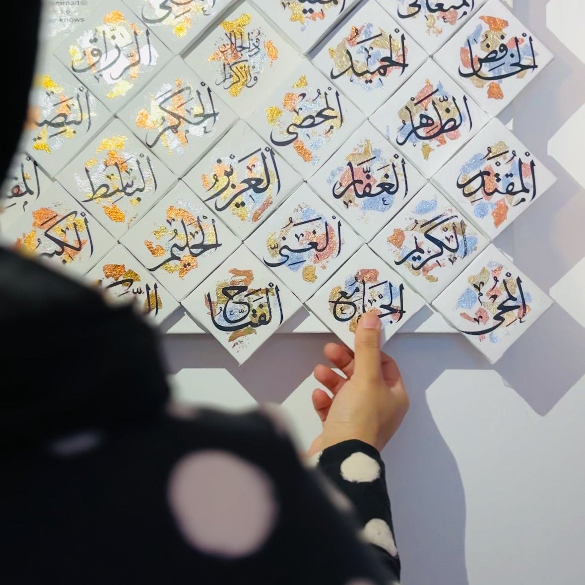 Hand interacting with Arabic calligraphy tiles on a light gray background