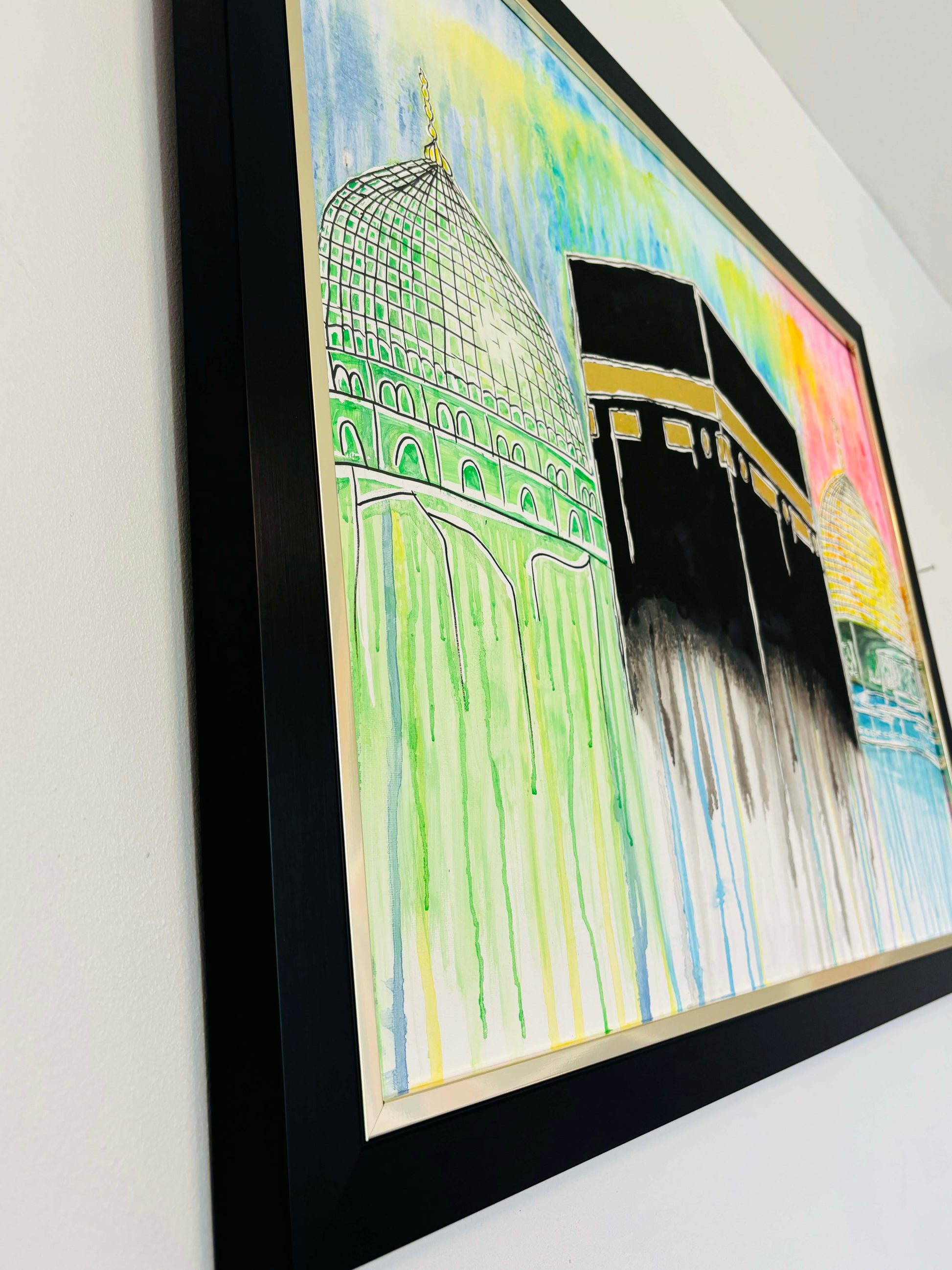Framed artwork of a colorful depiction of religious sites on a white wall.